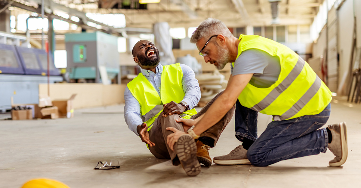 Two workers in an industrial workplace, wearing safety outfits, assisting after a workplace injury occurrence, illustrating the blog topic: Work-Related Personal Injury - When should you file a lawsuit?